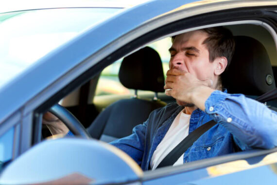 Man yawning behind the wheel of his car - cheap SR22 insurance.