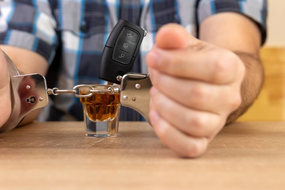 Hands are in hand cuffs with a shot glass full of liquor and a car key in the whiskey.