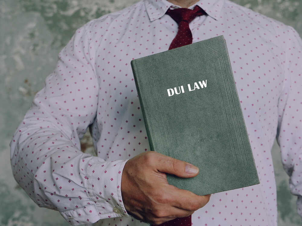 Man with shirt and tie holding a book that says "DUI Law".